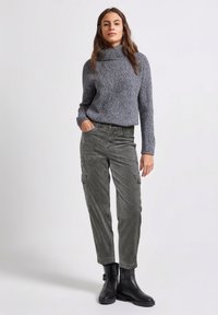 Szary sweter dziany z dekoltem typu komin, w zestawieniu z oliwkowymi spodniami typu cargo z bocznymi kieszeniami i czarnymi botkami za kostkę. Gładkie tekstury.