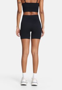 Crni sportski grudnjak i odgovarajuće visoko strukirane kratke hlače od elastične tkanine. Glatka tekstura, minimalni šavovi, i dužina do sredine butina.