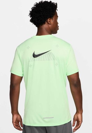 Mężczyzna o krótkich kręconych włosach, ubrany w jasnorozową koszulkę Nike z czarnym logo i wzorem kratki na plecach, zwrócony tyłem do kamery.