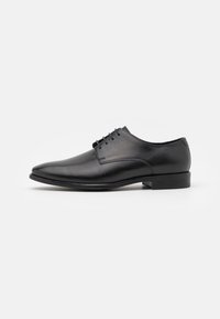 Chaussure habillée en cuir noir avec un bout pointu, texture lisse, cinq passants pour les lacets et un talon bas. Design épuré et minimaliste.