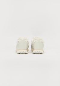 Lichtgekleurde sportschoenen met een gestructureerde stof en een glanzende leren bovenkant, met een gevoerde zool en contrasterende hakaccenten.