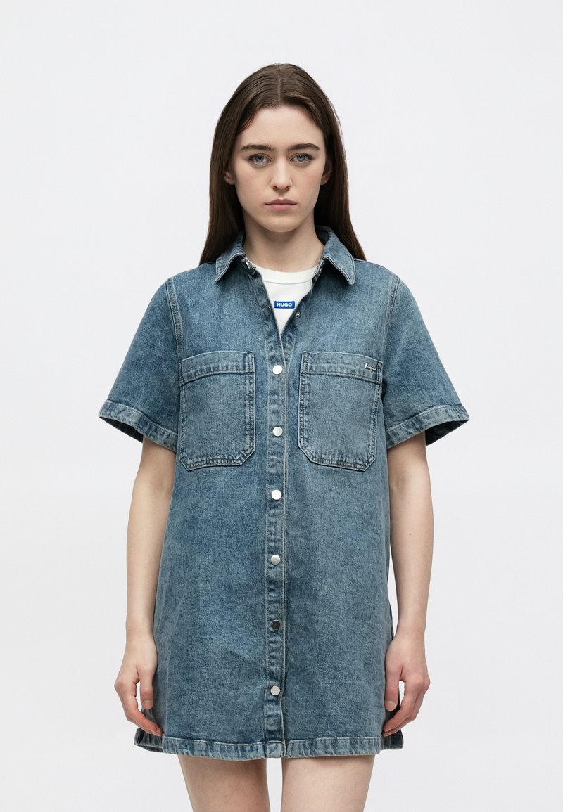 Φόρεμα πουκάμισο από τζιν με κοντά μανίκια σε ανοιχτό μπλε, με κούμπωμα με κουμπιά, δύο εμπρόσθιες τσέπες και ελαφρώς χαλαρή εφαρμογή, με ραμμένη τελειώματα και γιακά.