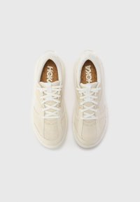 White sneakers with a textured mesh upper, thick white laces, and a cork insole. Features subtle gray accents and a rounded toe design.