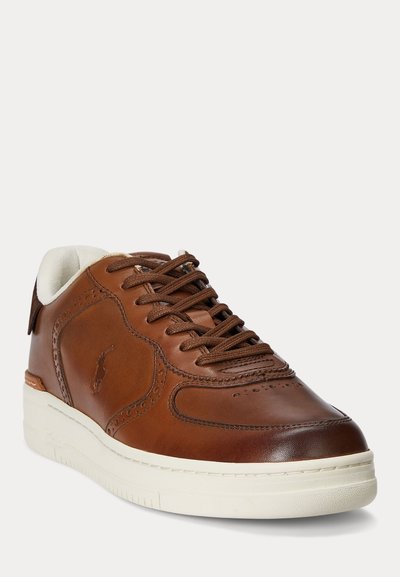 Barna bőrből készült sportcipő perforált részletekkel, barna fűzővel, fehér párnázott szegéllyel és vastag, törtfehér gumitalppal.