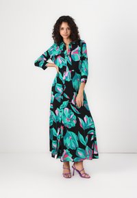 Robe maxi florale avec un fond noir, ornée de grands motifs de feuilles vertes et roses, avec un devant à boutons et des manches trois-quarts.
