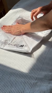 Weißes Kissen, das in transparentem Plastik eingewickelt ist, während Hände darauf drücken. Der Hintergrund zeigt einen strukturierten Stoff in hellgrauen und weißen Farbtönen.