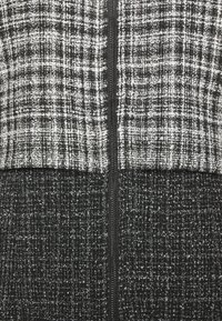 Gros plan d'un tissu en tweed noir et blanc avec une fermeture éclair noire verticale traversant le centre.