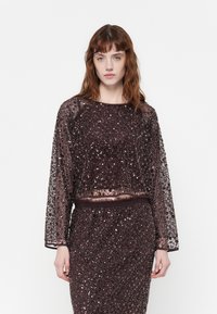 Doorzichtig, lang mouw cropped top versierd met donkere pailletten, met een ronde halslijn en elastische tailleband, gecombineerd met een bijpassende rok.