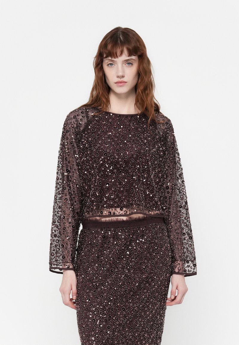 Haut court à manches longues en tissu transparent orné de sequins noirs, avec un col rond et une taille élastique, associé à une jupe assortie.