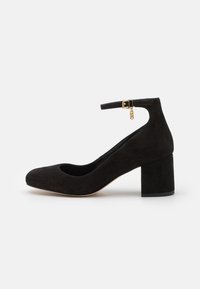Zapato de tacón de ante negro con punta redonda y correa para el tobillo. Presenta un tacón cuadrado y un acento de hebilla dorada. Textura suave, diseño minimalista.