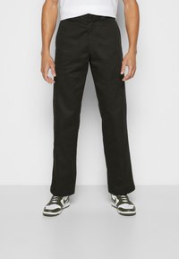Pantalons noirs à jambe droite en tissu de toile de coton avec une texture lisse. Associés à des baskets vertes et blanches, dotées de lacets.