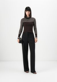 Mujer con cabello liso y oscuro que lleva una blusa de manga larga marrón con estampado, pantalones anchos negros, sandalias negras y sosteniendo un clutch negro.