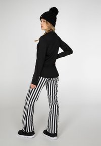 Top de manga larga negro, pantalones de campana a rayas en blanco y negro, y un gorro de punto negro con detalle de pom-pón. Zapatos negros con suelas blancas.