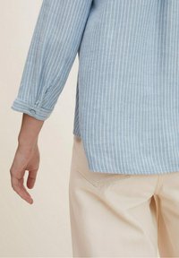 Camicia a righe blu chiaro con maniche lunghe, polsini abbottonati e orlo arrotondato, abbinata a pantaloni color crema.