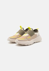 Αθλητικά παπούτσια με διχτυωτό και συνθετικό άνω τμήμα σε μπεζ και ελικοπράσινο χρώμα, με έντονες κίτρινες λεπτομέρειες και χοντρή λευκή σόλα.