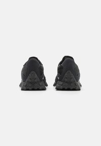 Baskets de sport noires avec un dessus texturé et des détails en maille, dotées d'une semelle extérieure triangulaire distinctive avec des grips circulaires.