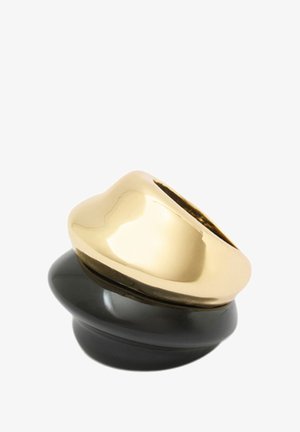 Złoty i czarny pierścień z gładkim, zaokrąglonym złotym wierzchem i wypolerowaną czarną podstawą, tworzący abstrakcyjny, warstwowy wzór.