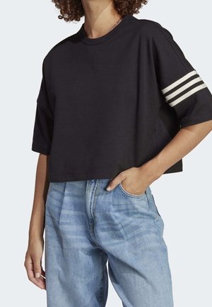 Person iført en løs sort cropped T-shirt med tre hvide striber på det ene ærme og lyseblå højtaljede jeans med løs pasform.