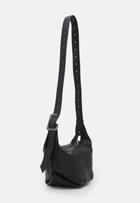 Sort læder skuldertaske med flad bund, justerbar perforeret rem og lynlås. Glat tekstur og minimalistisk design.