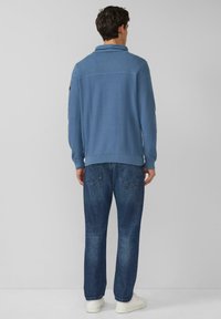 Jasnoniebieski sweter dziany z prążkowanym kołnierzem i tyłem, w połączeniu z ciemnymi dżinsami i białymi sneakersami. Nacisk na prostotę i wygodę.