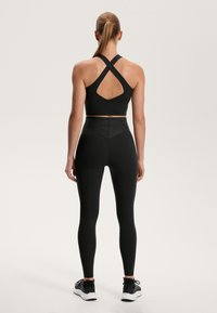 Čierny športový podprsenka s krížovými ramienkami a otvoreným chrbtom, spárovaná s čiernymi legínami s vysokým pásom. Hladká textúra a priliehavý strih.