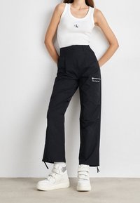 Svarta, högmidjade cargobyxor med sidofickor. Tillverkade av lättviktsmaterial, med en strukturerad yta och en vit logotypdetalj.