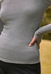 Graues, geripptes Langarmoberteil mit taillierter Passform. Verfügt über Daumenlöcher in den Bündchen, eine glatte Textur und einen dezenten Saum.