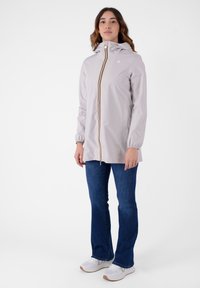 Jacca impermeabile grigia chiara con un design aderente, cappuccio e zip centrale con una striscia multicolore. Abbinata a jeans blu e sneakers.