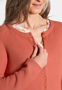Cardigan tricoté en corail avec un motif texturé, présentant un col rond, des fermetures à boutons et des poignets côtelés.