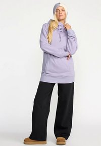 Lyse lilla hættetrøje med snor, forlommer og lange ærmer, kombineret med vide sorte bukser og tanfarvede støvler. Fremhævet med en strikket hue.