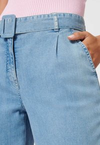 Hellblaue Jeanshosen mit einem taillierten Gürtel, Seitentaschen und einer glatten Textur. Der Stoff ist leicht verblasst mit dezenten Nähdetails.