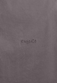 Gros plan sur un tissu marron avec le logo en relief "Khujo+Co" centré sur la surface.