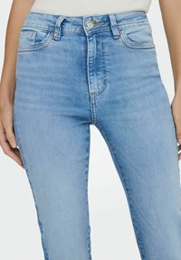 Šviesiai mėlynos džinsinės kelnės su aukštu liemeniu, penkių kišenių dizainu ir subtiliomis siuvimo detalėmis. Lygi tekstūra ir klasikinis kirpimas.
