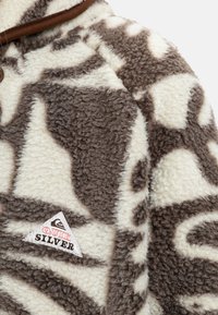 Fleece à demi-fermeture éclair en beige et brun, featuring des motifs abstraits et un logo Quiksilver sur un patch triangulaire sur le côté inférieur.