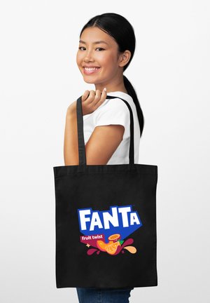 Czarna torba na zakupy z dużym, kolorowym logo Fanta, z napisem "fruit twist" oraz ilustracjami owoców, trzymana przez osobę w białej koszuli.