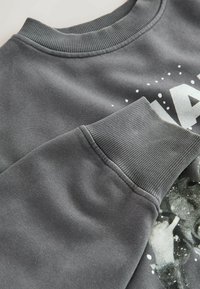 Szary sweatshirt z ribbowym dekoltem i mankietami, gładką fakturą oraz nadrukiem graficznym; szczegóły obejmują akcenty w kropki.