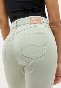 Lys grønne denimjeans har høy midje, baklommer med kontraststing og et lærmerke med "ANGELS" på linningen.