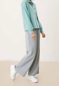Camisa polo de manga larga color azul claro con un bolsillo, combinada con pantalones de chándal grises holgados y zapatillas blancas. Tejido suave con un ajuste relajado.