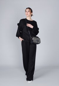 Conjunto de punto negro y texturizado con mangas con volantes; combinado con un pequeño bolso cruzado en blanco y negro. Ajuste suave y relajado.
