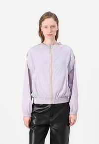 Licht lila jack met capuchon, volledige rits aan de voorkant, elastische manchetten en zoom. De stof lijkt glad en licht glanzend. Zwarte broek.