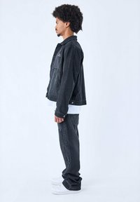 Chaqueta de mezclilla negra con grandes bolsillos frontales, acentos texturizados, combinada con pantalones de mezclilla negra a juego y zapatillas blancas.