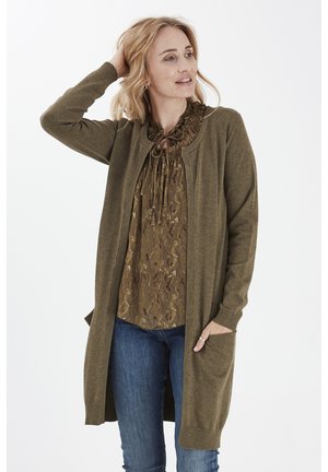 Olive roheline kudumiskardigan pika disainiga, soonikute äärtega ja avatud esiosaga. Kandestatud mustrilise pruun blousee peale, koos siniste teksadega.