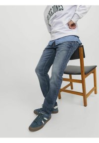 Sinised denim püksid kitsas sääres, millel on peened kulumise ja õmbluse detailid. Kombineeritud halli treeningpusa ja tumesiniste tossudega.
