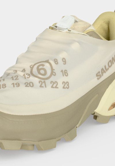 Μπεζ παπούτσι Salomon για μονοπάτι με ανθεκτική σόλα, αριθμημένο σχέδιο ημερολογίου στο επάνω μέρος και σύστημα γρήγορου δέσιμου.