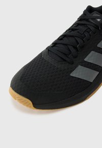 Black athletic shoe with mesh upper and rubber sole. Features three glossy black stripes on the side and a gum rubber toe cap.