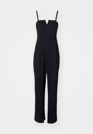 Combinaison noire avec un décolleté en V, des fines bretelles et un buste ajusté. Conception à jambes larges avec des plis qui ajoutent de la structure. Texture de tissu lisse.