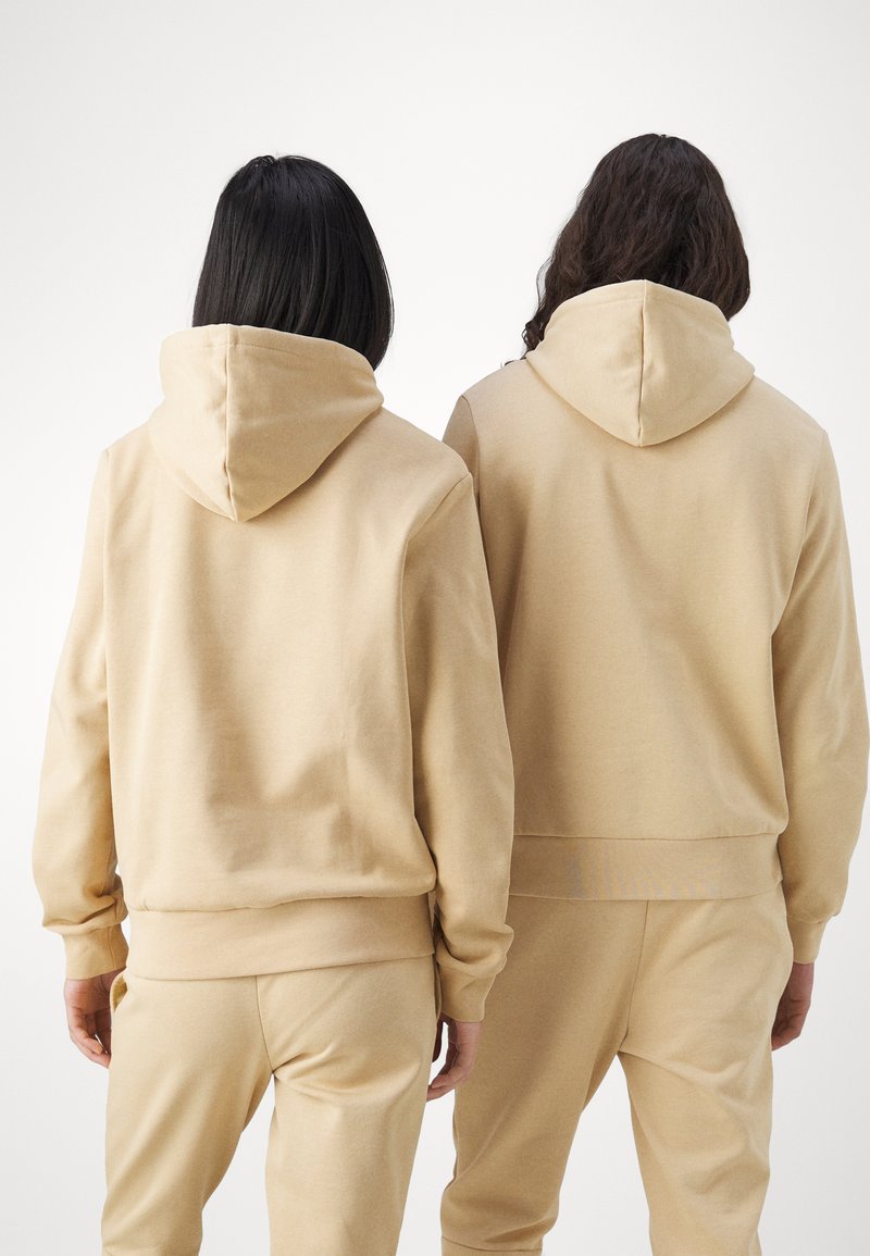 Beige Sweatshirts aus weichem Stoff, mit einer Kängurutasche und gerippten Bündchen, kombiniert mit passenden Jogginghosen. Ansicht von hinten.