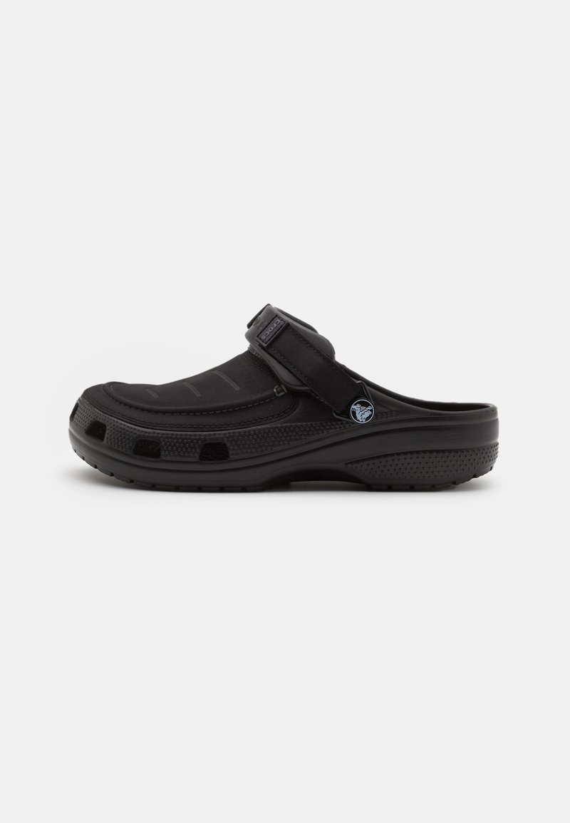 Black clog made of rubber with a textured surface and adjustable strap. Features ventilation holes and a contoured footbed for comfort.