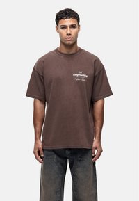 Bruine oversized t-shirt met korte mouwen van zachte katoen, met een klein wit logo op de borst en een relaxte fit.