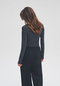 Langærmet bluse i kulgrå med figursyet silhuet, kombineret med løse sorte bukser med elastisk talje. Glat tekstur.